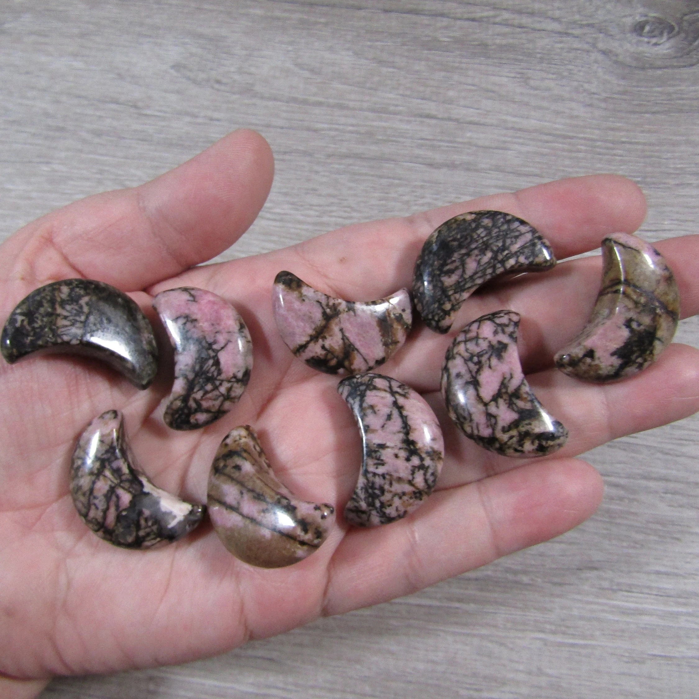 Rhodonite crescent moon for sale on a hand with a grey background - Keystone Crystals