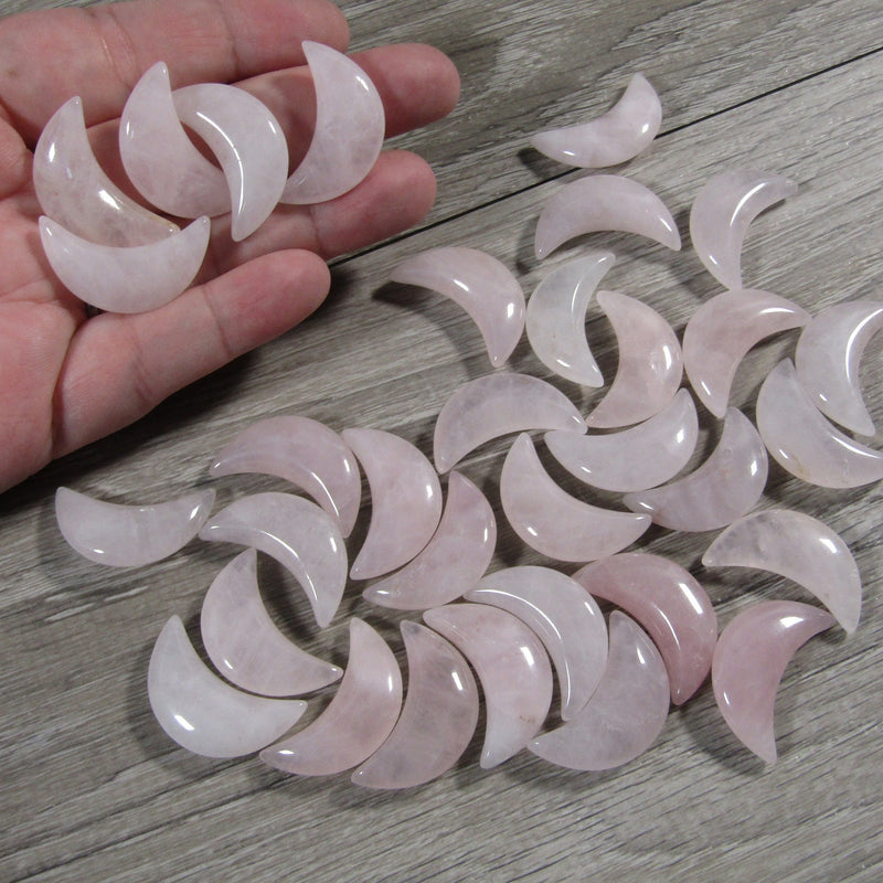 Wholesale rose quartz crescent moon displayed on a hand with a grey background - Keystone Crystals