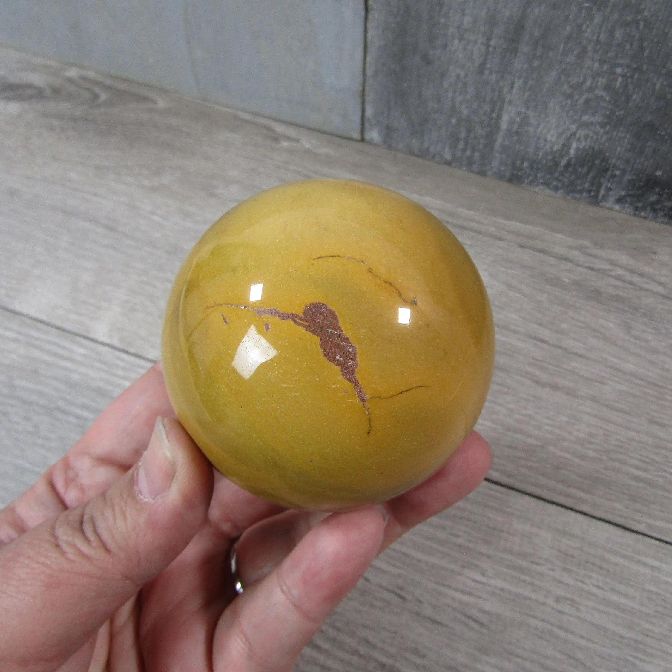 Hand holding a Large Mookaite Jasper Sphere to show size and polished finish.